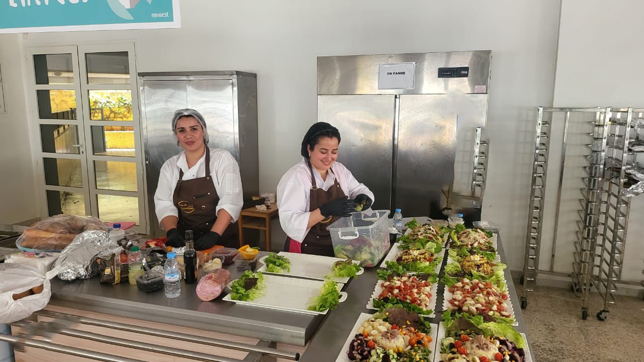 Deux chefs préparant des plats dans une cuisine, entourés de salades colorées.